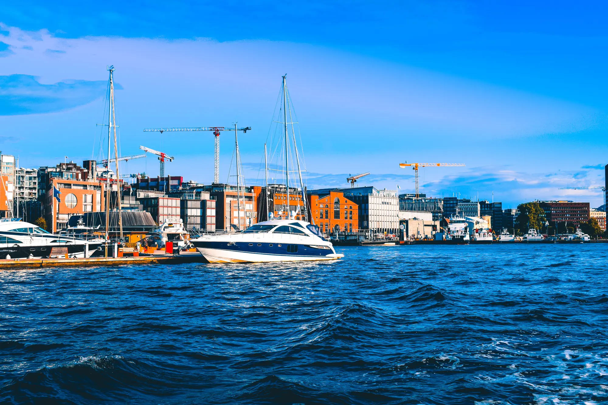 A white motor yacht moored in Oslo harbour in front of the city waterfront on a clear day.